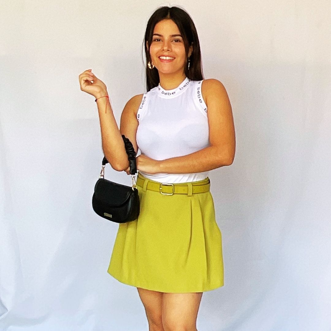 Outfit de mujer con top blanco, falda verde lima y cartera negra.